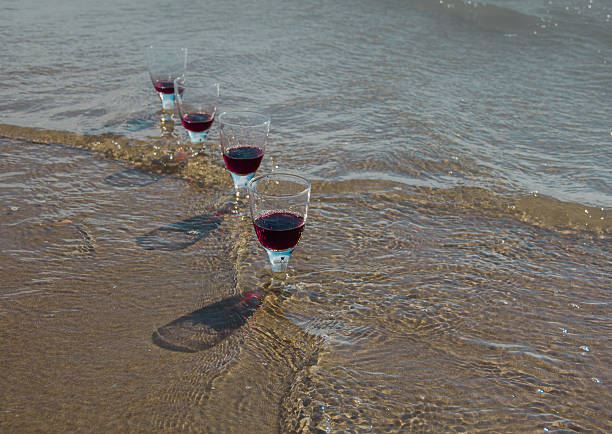 Four glasses with red wine in the waves of the sea coast